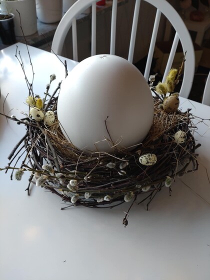 Stor vit dekorationsägg i ett fågelbo av kvistar och små prydnadsägg på ett vitt bord.