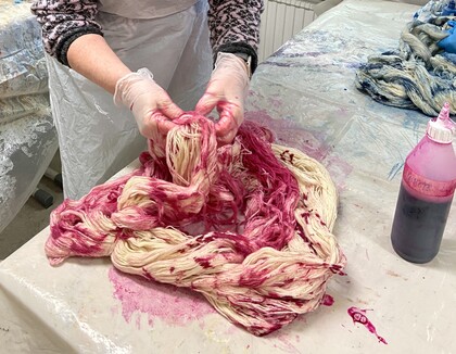 Person färgar garn rosa för hand på ett bord täckt med plast.