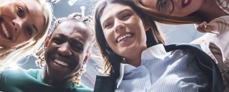 En grupp glada människor står i en cirkel och tittar ner mot kameran, fotograferade underifrån.