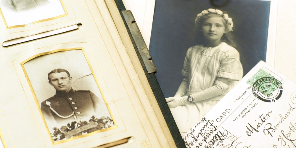 Ett gammalt fotoalbum, ett porträttfoto av en flicka, vykort och ett fickur i guld på ett bord.