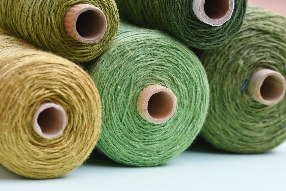 Fem stora rullar garn i olika gröna och gula nyanser ligger staplade på varandra.