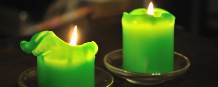 Två gröna stearinljus brinner på små glasfat på ett mörkt bord.