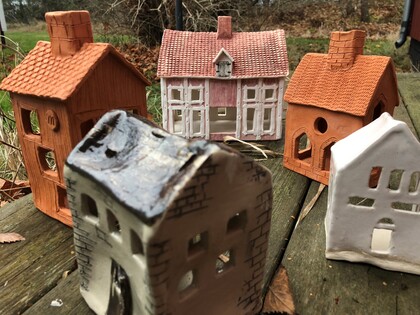 Fem små keramikhus står på ett träbord utomhus, omgivna av höstlöv och natur.