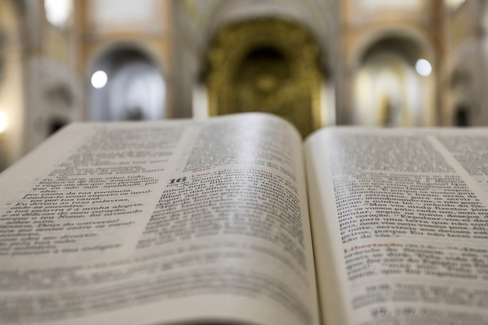 En uppslagen bok, troligen en bibel, ligger i fokus i en kyrka med suddig bakgrund.