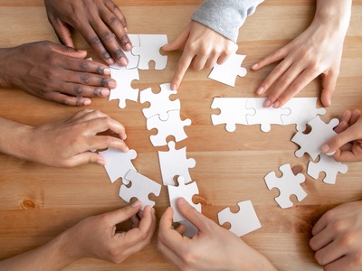 Flera händer samarbetar för att lägga ett pussel på ett trägolv.