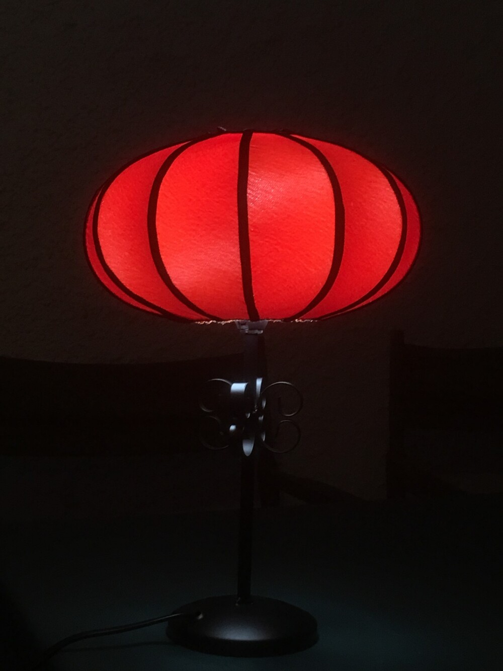 En bordslampa med röd, rund lampskärm som lyser i mörk miljö.
