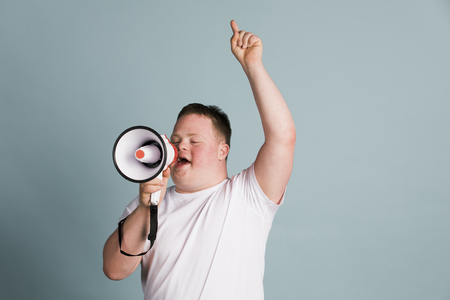Person i vit t-shirt håller en megafon och pekar uppåt mot en ljusblå bakgrund.