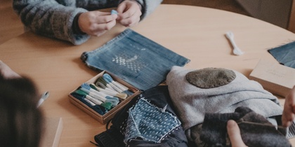 Tre personer sitter runt ett bord och arbetar med tygbitar och broderimaterial.