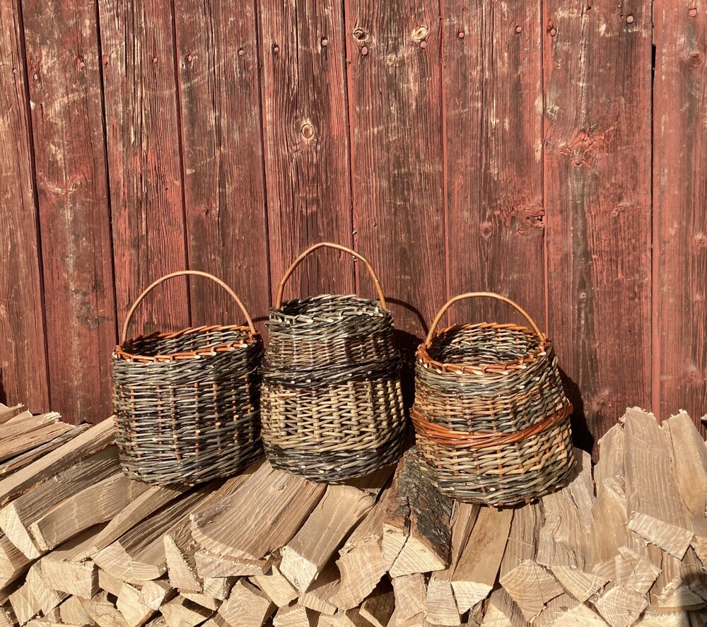 Tre flätade korgar står på en stapel ved framför en röd trävägg.