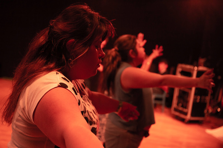 Två personer står med utsträckta armar i en scenmiljö med varm belysning.