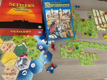 Två sällskapsspel, Settlers från Catan och Carcassonne, uppdukade på ett bord med spelbrickor och pjäser.