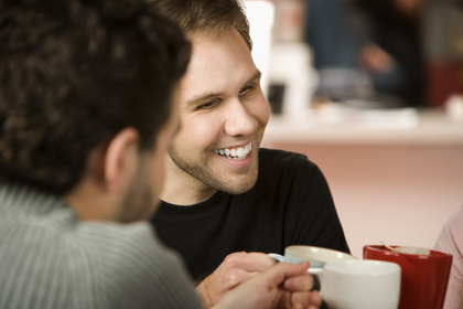 Två personer sitter på ett café och samtalar glatt över varsin kopp kaffe.