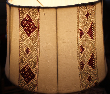 Närbild av en lampskärm med broderade och virkade mönster i beige och vinrött.
