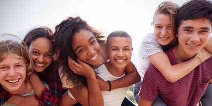 Sex ungdomar utomhus, två ger ryggsäckar till sina vänner, alla ler mot kameran.