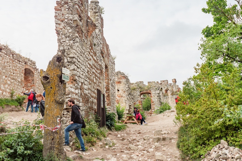 Ruiner av en gammal stenbyggnad med flera personer som promenerar bland stenarna och grönska.
