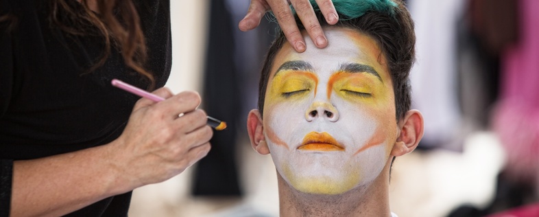 En person får ansiktsmålning med färgglada färger av en annan person, ögonen är slutna.