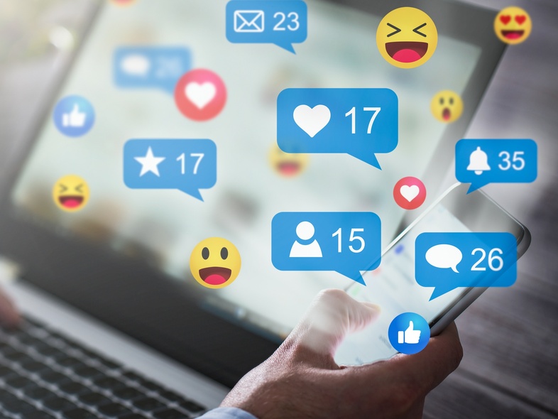 En person använder både en laptop och en smartphone med sociala medie-ikoner och notiser på skärmen.