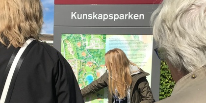 Tre personer står framför en informationsskylt vid Kunskapsparken, SLU, under en solig dag.