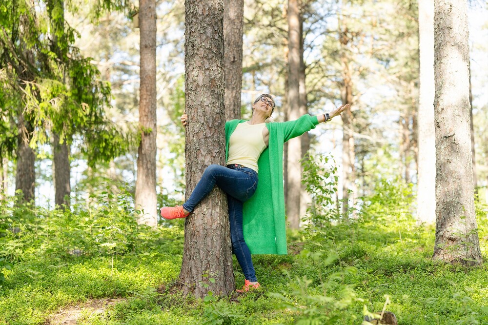 Person i grön kofta klättrar på ett träd i en solig skog.