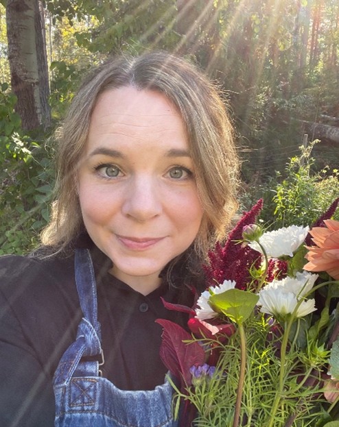 Person i trädgård håller en bukett färgglada blommor i solljus.