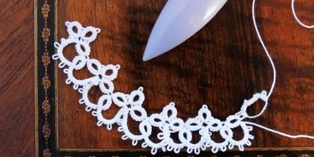 En skyttel och spetsarbete frivoliteter i vitt garn på ett träbord.