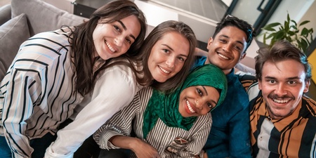 Fem unga vuxna sitter nära varandra i en soffa och ler mot kameran.