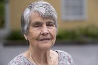 Bild av äldre kvinna med grått hår och suddig bakgrund.