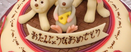 Dekorerad tårta med figurer av en kanin, en mus och en hund samt japansk text.
