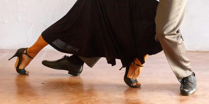 Ett par dansar tango i en elegant pose mot en ljus vägg.