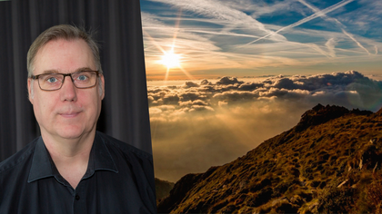 En person i svart skjorta står framför ett mörkt draperi, bredvid ett landskap med solnedgång över moln och berg.