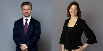 En man i kostym och en kvinna i svart kavaj poserar mot en grå bakgrund.