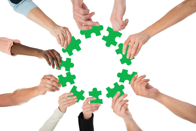 Flera händer håller gröna pusselbitar i en cirkel mot en vit bakgrund.