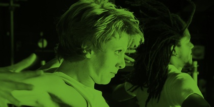 Två personer dansar energiskt med utsträckta armar, belysta av grönt ljus.