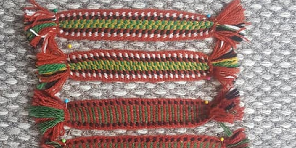 Fyra handvävda band i olika färger ligger på en grå matta.