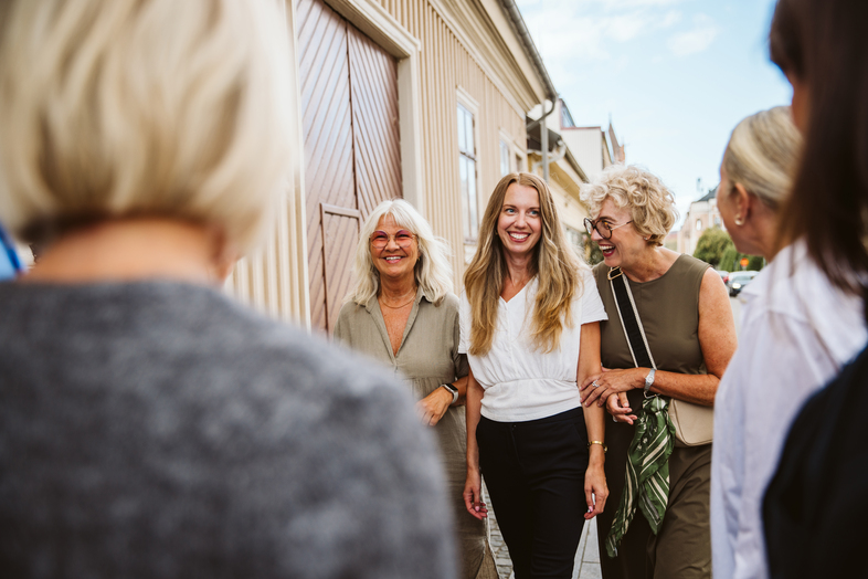 Tre kvinnor går arm i arm och ler