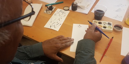 En person övar kalligrafi vid ett bord med papper, bläck och penslar.