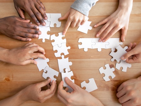 Flera händer samarbetar för att lägga ett pussel på ett trägolv.