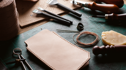 Ett arbetsbord med verktyg och material för läderhantverk, inklusive nålar, tråd och läderbitar.