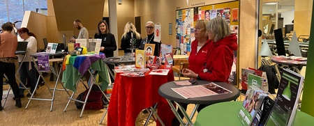 Mässa med informationsbord och människor i en modern inomhusmiljö, dekorerat med färgglada stjärnor.