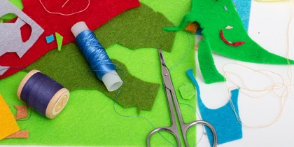 Färgglada tygbitar, trådrullar och en sax på ett bord, material för sömnad eller pyssel.