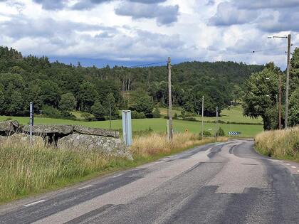Landsväg som slingrar sig genom ett grönt landskap med skog, ängar och molnig himmel.