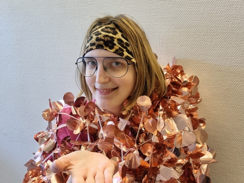 Person med leopardmönstrat hårband och glänsande dekorationer sträcker ut handen mot kameran.