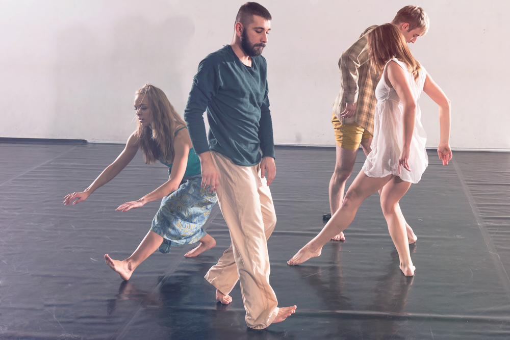 Fyra personer dansar barfota på ett svart golv i en ljus dansstudio.
