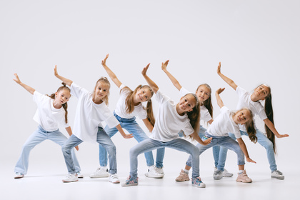Sju barn i vita t-shirts och jeans dansar tillsammans i en grupp mot vit bakgrund.