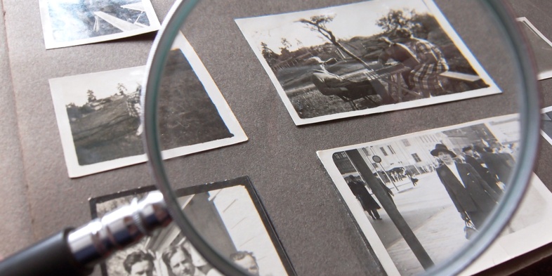 Ett fotoalbum med svartvita fotografier granskas med ett förstoringsglas.