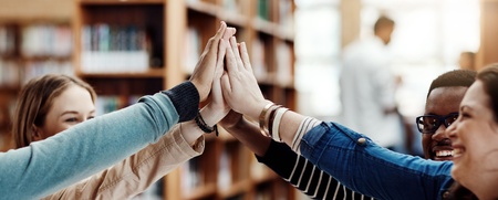 Fyra unga personer gör en high five tillsammans i ett bibliotek.