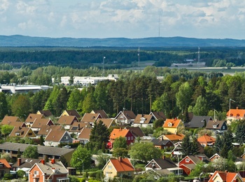 Färgglada villor med röda och gula tak i ett lummigt bostadsområde, omgivna av skog och berg i bakgrunden.