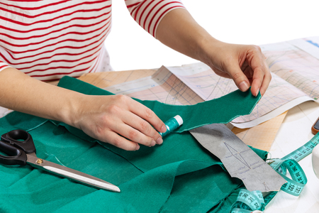 En person markerar tyg med krita, omgiven av mönsterpapper, sax och måttband på ett bord.