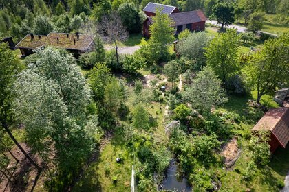 Flygfoto över en grönskande trädgård med flera röda hus, träd, buskar och en damm.