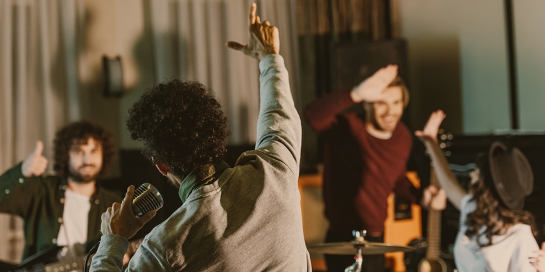 Ett band repeterar i en studio, sångaren sjunger i mikrofon och bandmedlemmar spelar instrument och hejar på varandra.